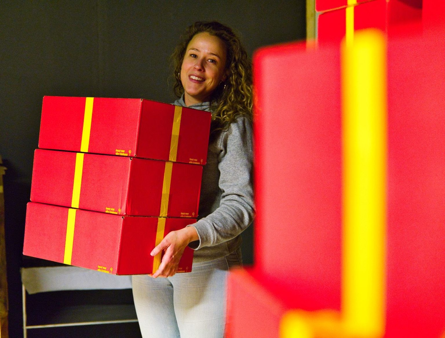 Vrijwilliger met gestapelde rode Sinterklaaspakketten van Feest voor alle kinderen.